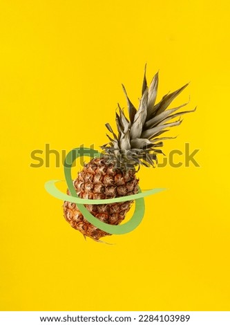Ripe pineapple with green paper hoops against a yellow background. Minimalistic creative fruit concept. Vertical frame.
