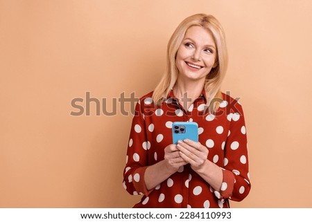 Photo of positive dreamy woman with bob hairdo wear dotted shirt look empty space hold smartphone isolated on pastel color background