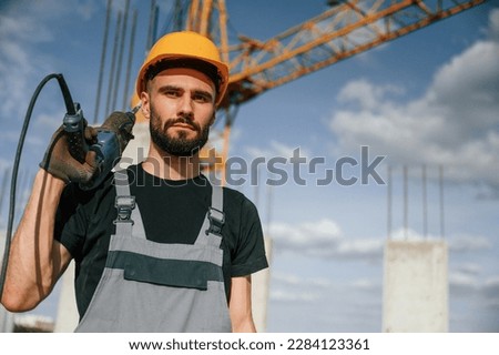 Portrait of man that is in uniform with the drill on the construction site.