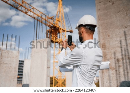 Taking a picture of place by smartphone. Man in uniform is working on the construction site.