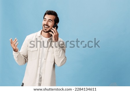 Portrait of a man brunette animation and joy talking on the phone hand up from surprise victory and happiness smile with teeth, on a blue background in a white T-shirt and jeans, copy space