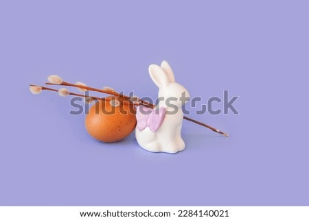 Spring easter holiday, decorative composition with willow branch, white statuette rabbit and colorful painted eggs on pastel light blue background. Isolated, front view, place for text or logo