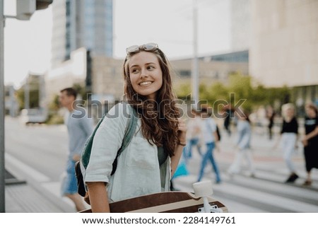 Young woman walking in city with skateboard. Youth culture and commuting concept.