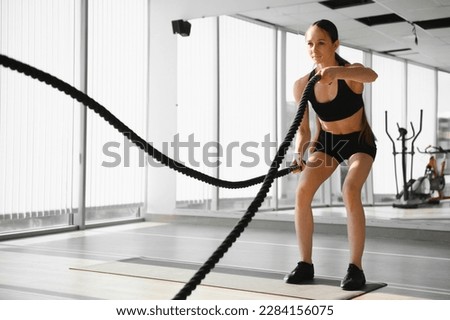 Athletic Female in a Gym Exercises with Battle Ropes During Her Fitness Workout High-Intensity Interval Training. She's Muscular and Sweaty. Royalty-Free Stock Photo #2284156075