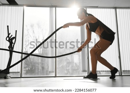 Athletic Female in a Gym Exercises with Battle Ropes During Her Fitness Workout High-Intensity Interval Training. She's Muscular and Sweaty. Royalty-Free Stock Photo #2284156077
