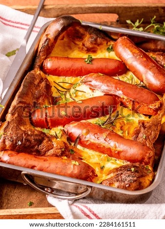 British Toad in the hole, with fresh parsley and rosemary sprigs. Baked sausages in Yorkshire pudding are a perfect breakfast idea