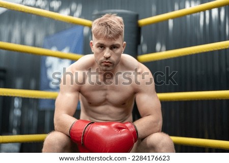 Man boxer sitting in corner on boxing ring at gym. Male MMA fighter looking competitor between rounds.