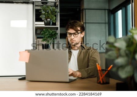 Focused young businessman study online watching webinar podcast on laptop listening learning education course conference calling make notes sit at work desk, elearning concept