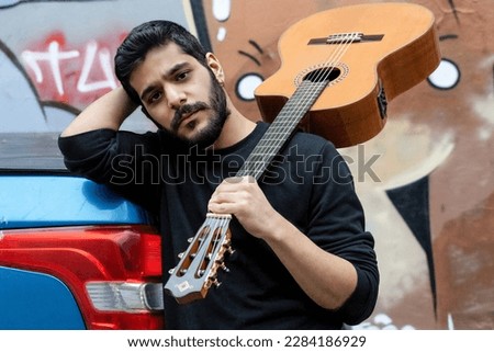 Guitarist with her guitar on his shoulder leaning on the end of a blue pickup truck, posing for a cover photo of the artist.