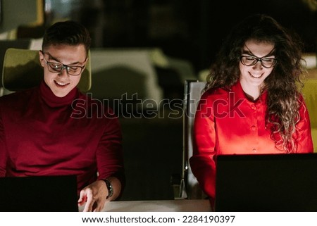 A front view photo of young beautiful male and female coworkers working late at night in the office. They are having fun conversation and smiling