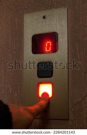 A finger presses the button to call the elevator.