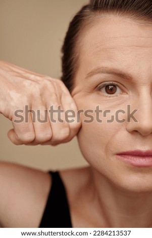 Face of mature woman pulling back skin of her face to get rid of wrinkles Royalty-Free Stock Photo #2284213537