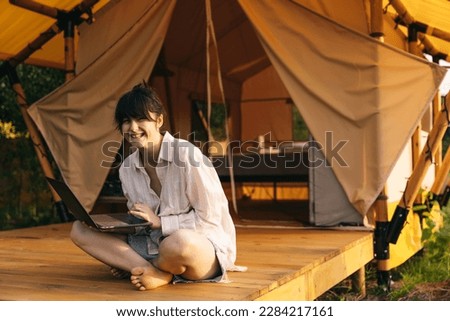 female traveler sitting beside camping tent and using notebook laptop computer working 