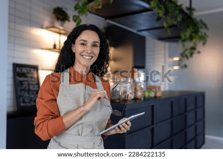 Portrait of young beautiful woman small business owner of coffee shop and cafe restaurant, Hispanic woman smiling and looking at camera with tablet computer and apron, successful woman boss. Royalty-Free Stock Photo #2284222135