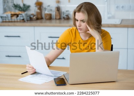 Caucasian woman analyzing budget or utility bills, looking worried sitting at home at the kitchen. Problems concept. 