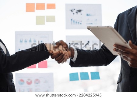 Close up of african american male with tablet shaking hands with caucasian female in formal wear on office background. Executive managers coming to agreement about marketing scheme in meeting room.
