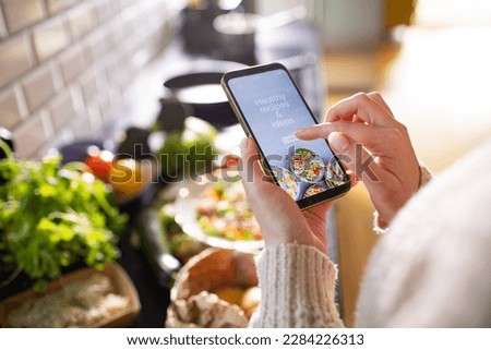 Young adult woman using a diet app on her phone while preparing a salad Royalty-Free Stock Photo #2284226313