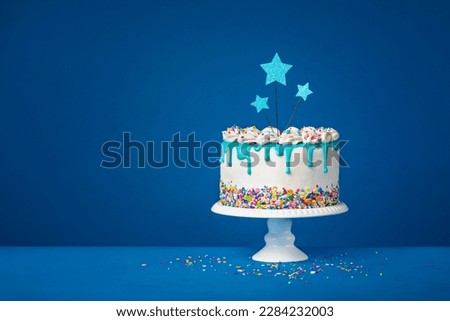White birthday drip cake with teal ganache, star toppers over dark blue background Royalty-Free Stock Photo #2284232003