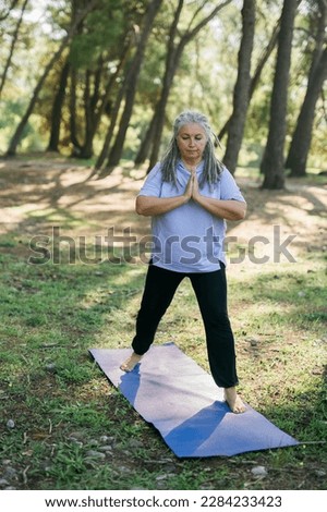 Senior woman with dreadlocks in stretching position on nature at morning. Elderly woman doing yoga on park - wellbeing and wellness tai chi
