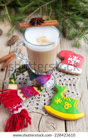 A glass of warm cacao with a small knit scarf and homemade gingerbread in the form of a red boot and a green horse on a wooden table. Selective Focus on glass