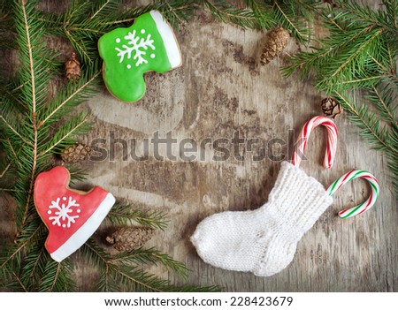 Homemade christmas gingerbreads painted as a red hat and green boot and and small knitted sock with candy canes on the wooden background with fir branches. Selective focus and place for text. Toned