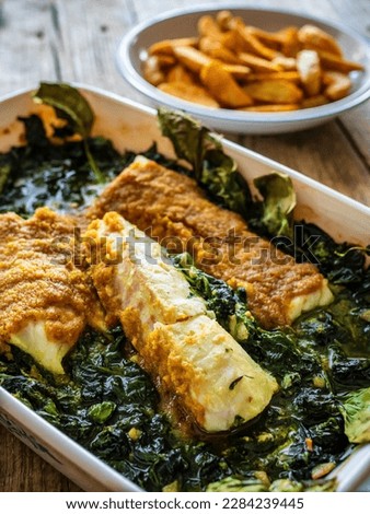 Fish dish - roast cod fillet with potatoes and spinach served on stone plate on wooden table 