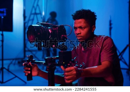 Young African American camera operator shooting on professional camera in dark studio Royalty-Free Stock Photo #2284241555