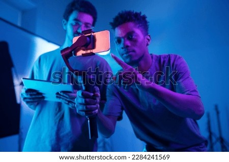 African American operator using special technique to shoot video on smartphone with his colleague using digital tablet Royalty-Free Stock Photo #2284241569