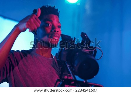 Operator of production studio showing thumb up to his team while standing in front of camera during shooting