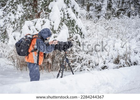 Professional Cameraman with camera shooting natural footage in snow forest. Behind scene concept