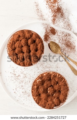 Homemade eggless Tiramisu, traditional Italian dessert in single-portion glass cups on white background. Top view Royalty-Free Stock Photo #2284251727
