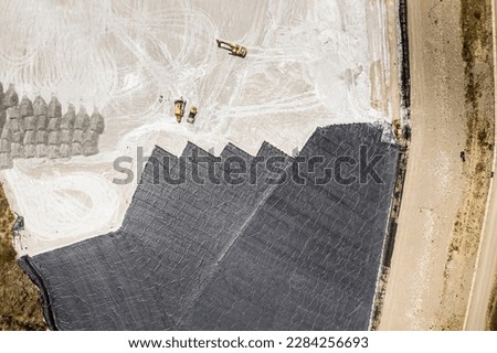 Aerial view of remediation work on a terrain with mining waste fillings, where working machinery and high-density geomembrane cover can be seen. Royalty-Free Stock Photo #2284256693