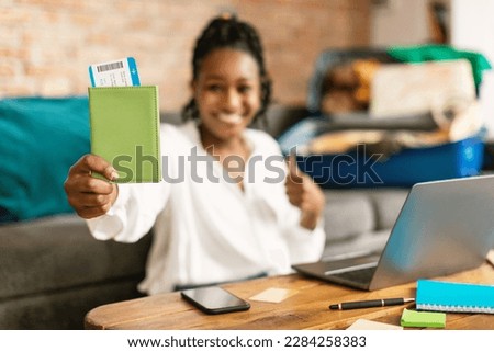 Excited black woman advertising cheap travel tickets offer, holding passport and boarding pass, showing thumb up and smiling, selective focus. Vacation and tourism concept