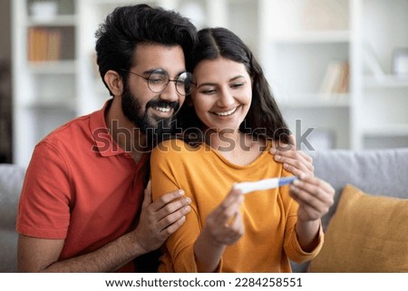 Portrait Of Happy Young Indian Couple Looking At Positive Pregnancy Test While Sitting Together On Couch At Home, Loving Millennial Eastern Spouses Awaiting Baby, Becoming Parents, Free Space Royalty-Free Stock Photo #2284258551