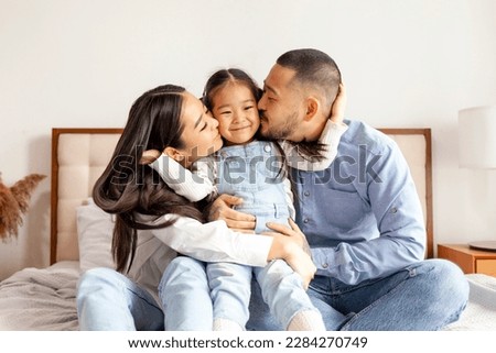happy young asian family sit on bed together with daughter, korean little girl hug and love parents at home, mom and dad kiss daughter Royalty-Free Stock Photo #2284270749