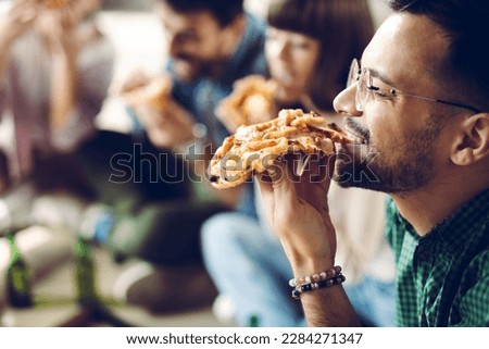 Close up of young man enjoying while eating pizza with his friends  