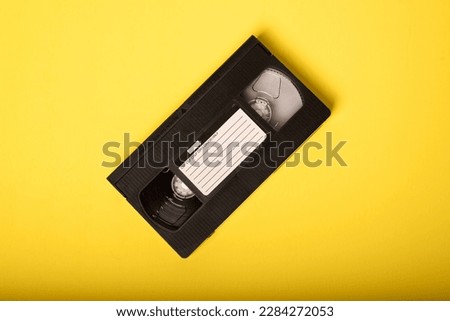 Movie Night - Video Tape on Yellow Background. VHS Tape, a staple of an age before streaming, when movie rental stores were a necessary element of watching a movie at home. Royalty-Free Stock Photo #2284272053