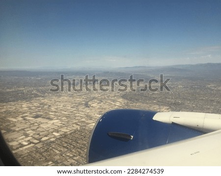 From the plane, Los Angeles is a sprawling cityscape of palm-lined streets, modern high-rises, historic buildings, and famous landmarks like the Hollywood sign and Griffith Observatory. The blue sky a