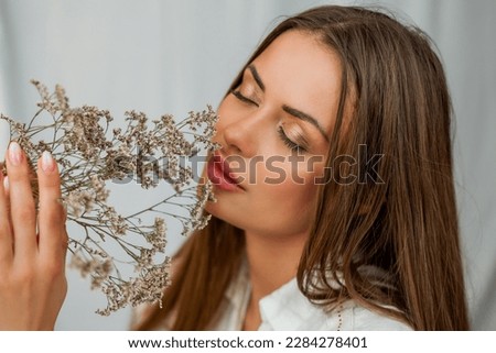 Portrait of beautiful young woman with long hair on white background with dried flowers.