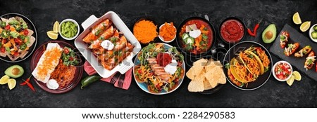 Mexican food table scene. Top down view on a dark stone banner background. Tacos, burrito plate, nachos, enchiladas, tortilla soup and salad. Royalty-Free Stock Photo #2284290583