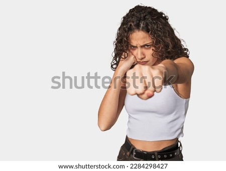Radiant young woman with stunning curls throwing a punch, anger, fighting due to an argument, boxing.