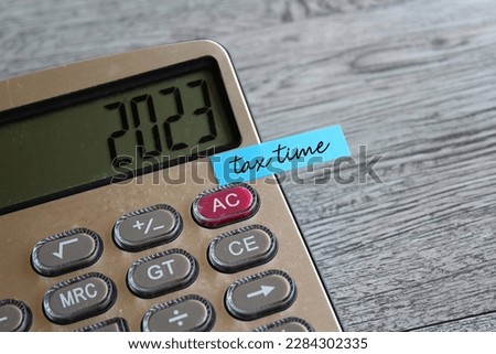 Close up image of calculator with number 2023 on display and sticky note with text TAX TIME. Finance concept