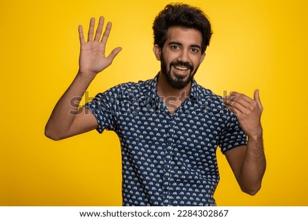 Come here, join us. Welcome. Hindu bearded man showing inviting gesture with hands, ask to join, beckoning to coming, gesturing hello, goodbye. Handsome indian guy isolated on yellow studio background Royalty-Free Stock Photo #2284302867