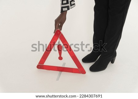 England, UK. 2022.  Woman driver placing a red danger triangle to warn oncoming traffic  of  a motoring situation ahead,