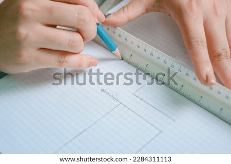 close-up of female white hands making a line on a grid sheet with a scale ruler and a graphite pencil, interior design and architecture work. copy space.