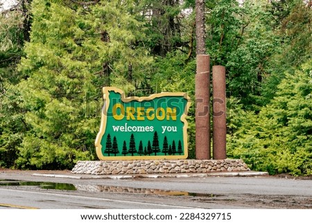 Oregon welcomes you sign after hard rain with puddle as seen from across US-199.