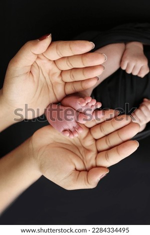 The palms of the parents. A mother hold the feet of a newborn child in a black blanket on a Black background. The feet of a newborn in the hands of parents. Photo of foot, heels and toes
