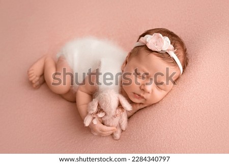 Top view of a newborn baby girl sleeping in a white jumpsuit with pink rabbit a white bandage and a pink flower on her head on a pink background. Beautiful portrait of a little girl 7 days, one week. Royalty-Free Stock Photo #2284340797