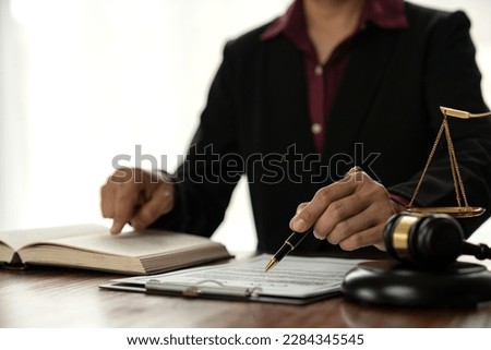 Female lawyer or legal counsel sitting at desk reading and reviewing data in file folder, legal book in accordance with the principles of jurisprudence to study and find information. Royalty-Free Stock Photo #2284345545