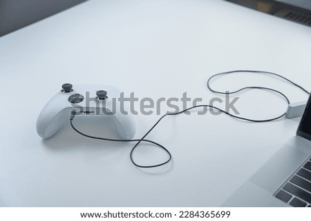 Stylish gameplace with modern gadgets. Emty gamespace with gamepad for gamers. Remote job. Laptop and big screen on a desk. Close-up of closed laptop on white table against the window. 